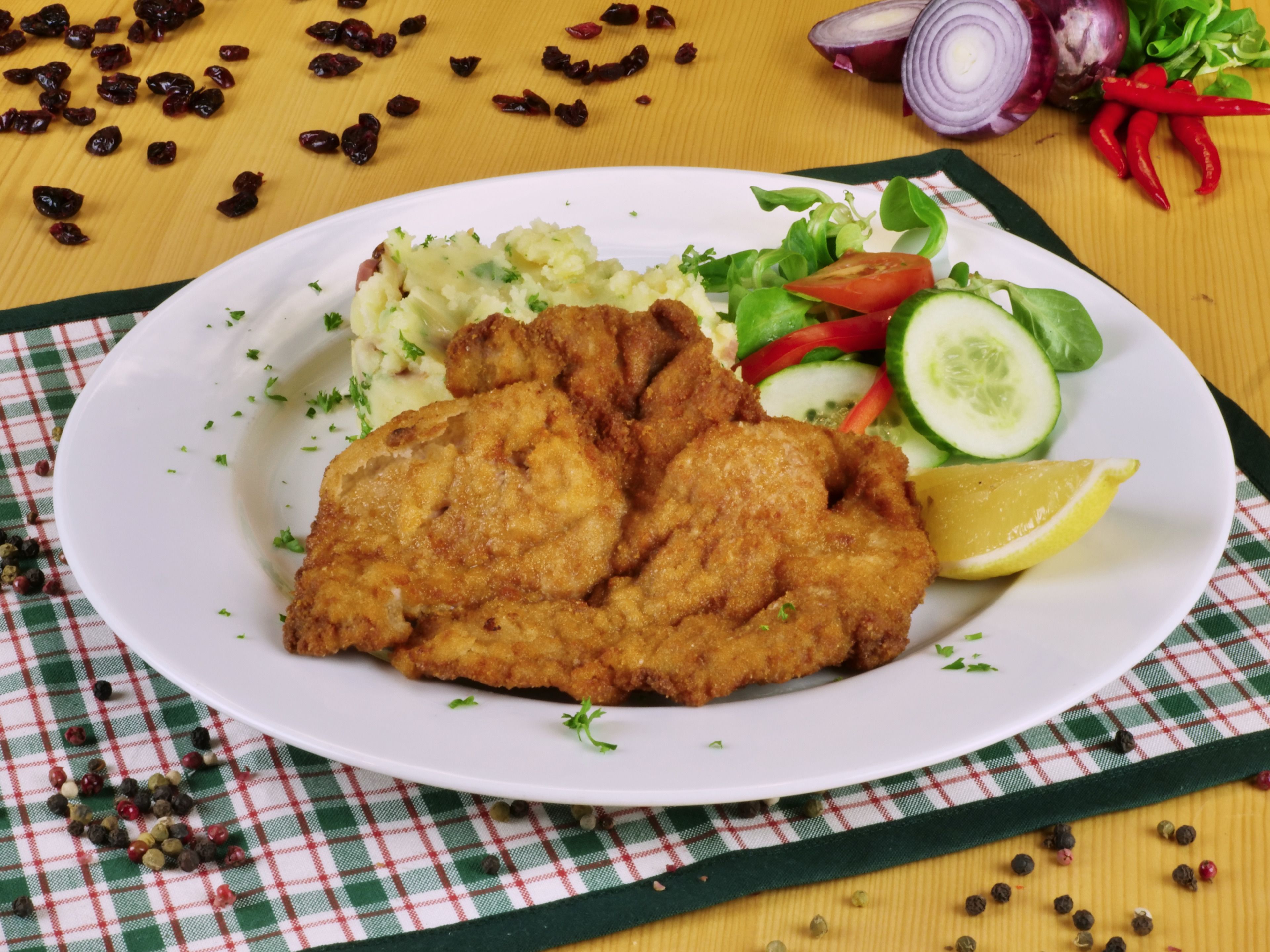 A plate of fried fish, salad, and lemon on a checkered tablecloth.