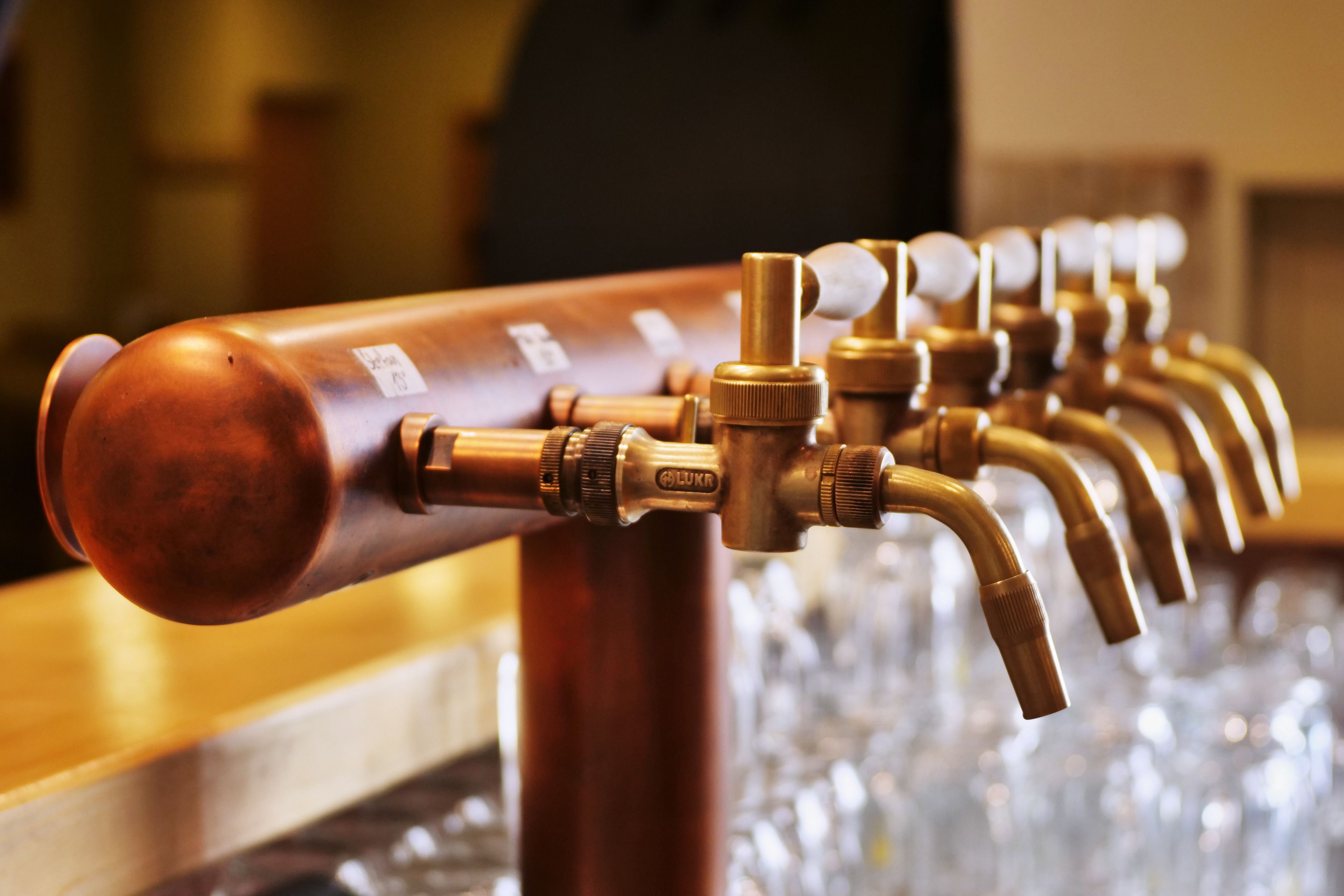 A row of copper beer taps with a label reading "LUKR" on a bar counter.