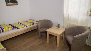 A small, cozy room with a single bed, a chair, a table, and a picture on the wall.