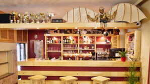 Een bar met houten krukken, flessenrekken en een decoratief figuur aan het plafond.