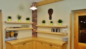 Een hoekkeuken met houten kasten, een accentmuur van baksteen en planken met planten en keukengerei.