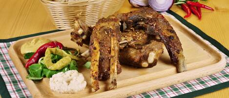 A wooden cutting board with roasted chicken, bread, and salad.