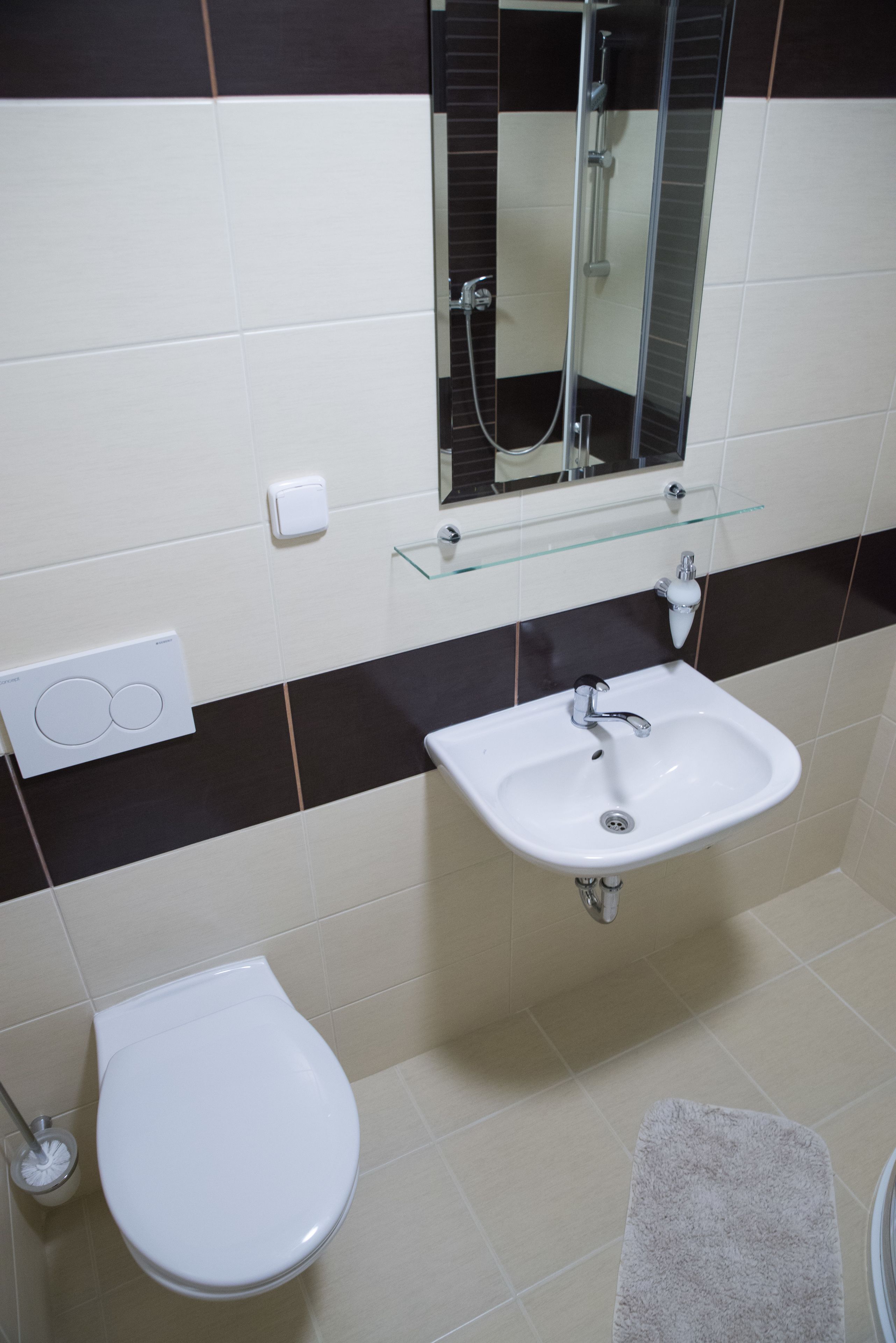 A bathroom with a white toilet, a white sink, a glass shelf above the sink, a mirror, and a towel on the floor.