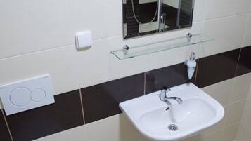 A bathroom with a white toilet, a white sink, a glass shelf above the sink, a mirror, and a towel on the floor.