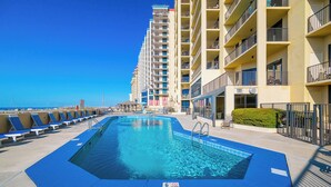 A swimming pool with lounge chairs, a building with balconies, and a clear sky. - Beautiful 3BR Condo - Phoenix IV 4075 (Orange Beach)