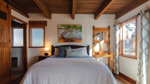 A bedroom with a large bed, wooden beams, a painting, a nightstand, a lamp, and a window with curtains.