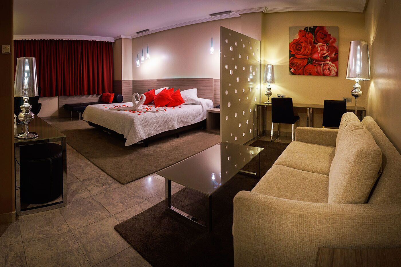 Une chambre d’hôtel avec un lit, un canapé, un bureau et un mur orné d’un tableau représentant des roses.