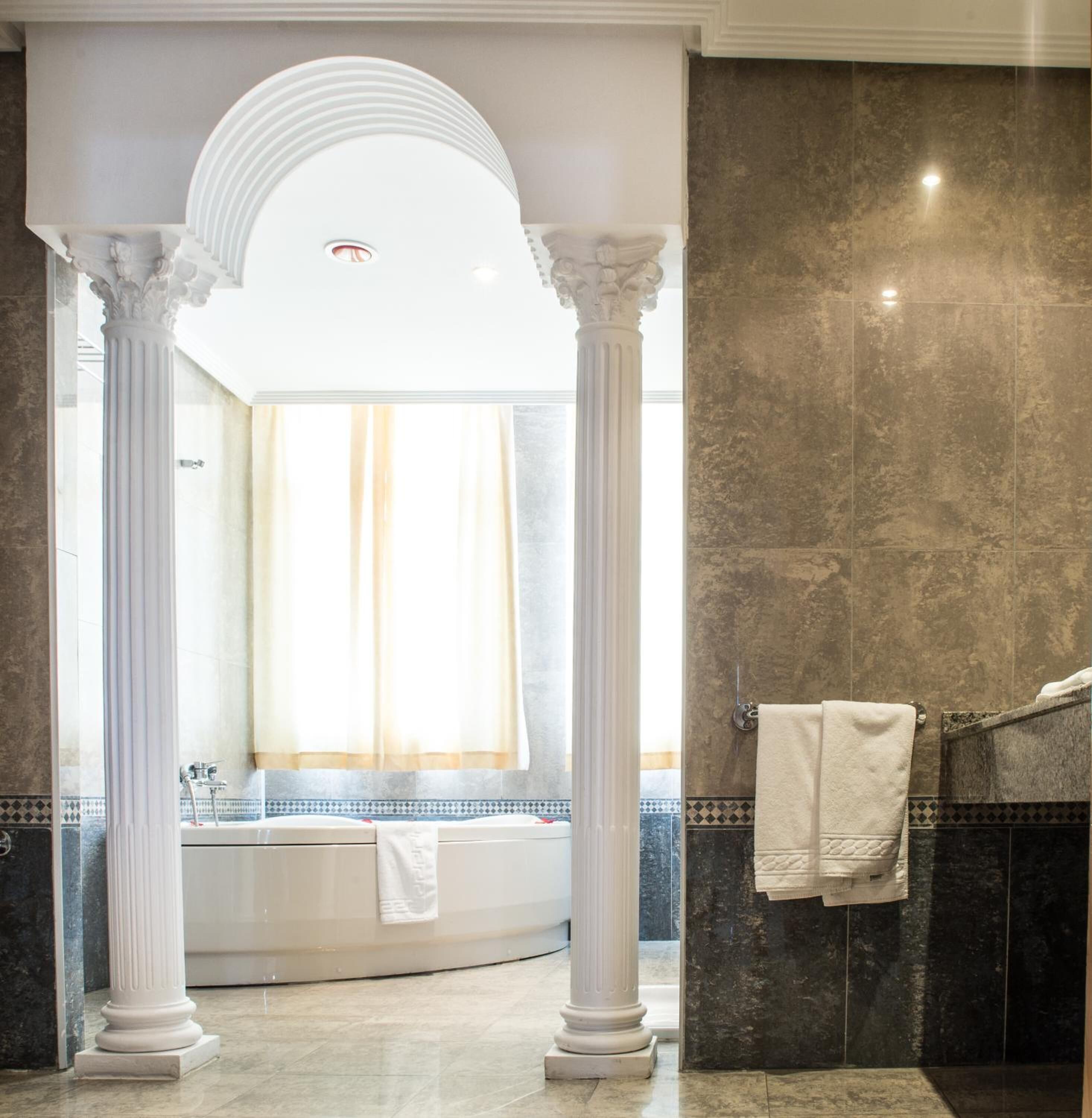 Un baño lujoso con una bañera independiente, piso de mármol y un ventanal con cortinas.