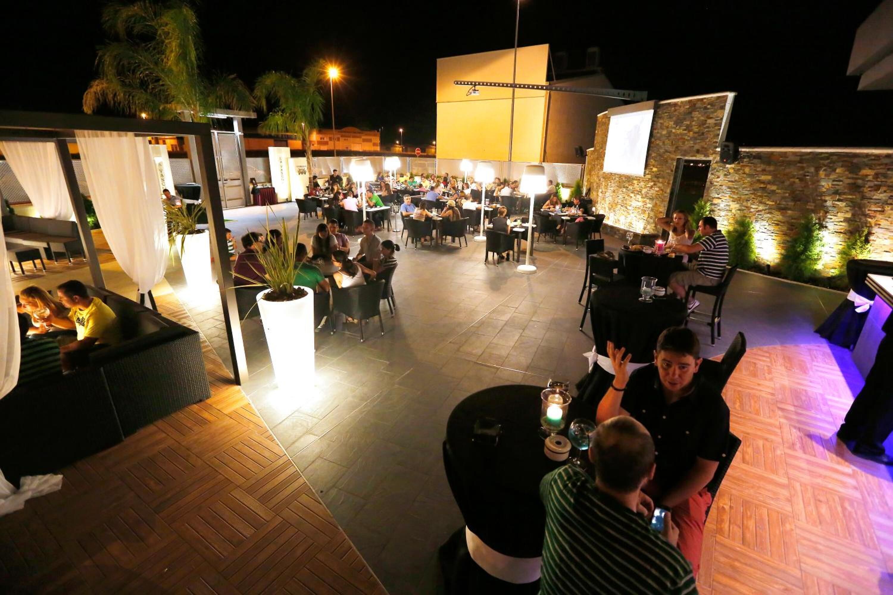 An outdoor dining area with multiple tables and chairs, surrounded by a stone wall and a wooden deck.