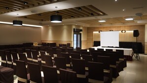 Un salón de conferencias con filas de sillas, una pantalla de proyector y un orador.