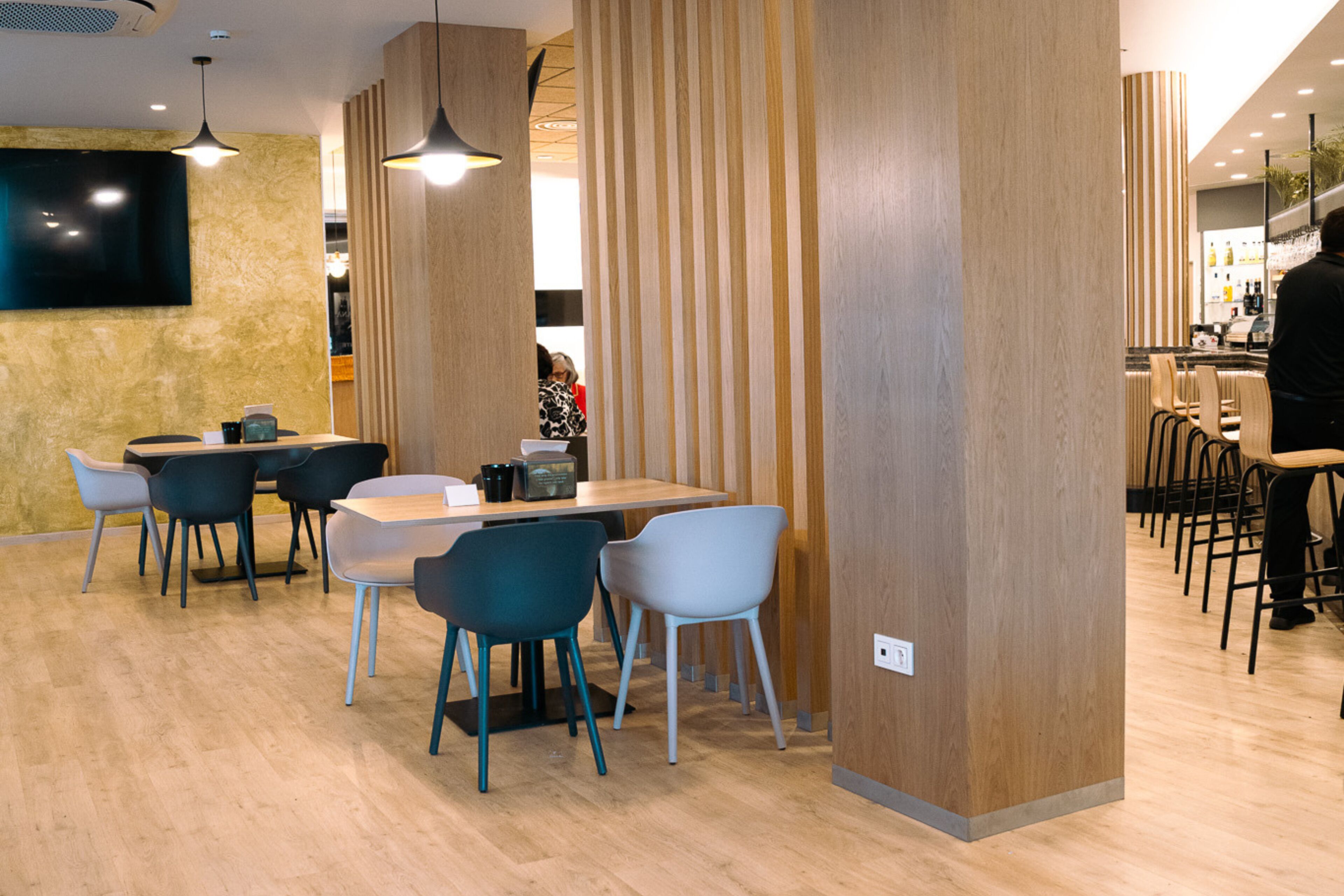 Un restaurante moderno con paneles de madera, una zona de bar y un televisor de pantalla plana en la pared.
