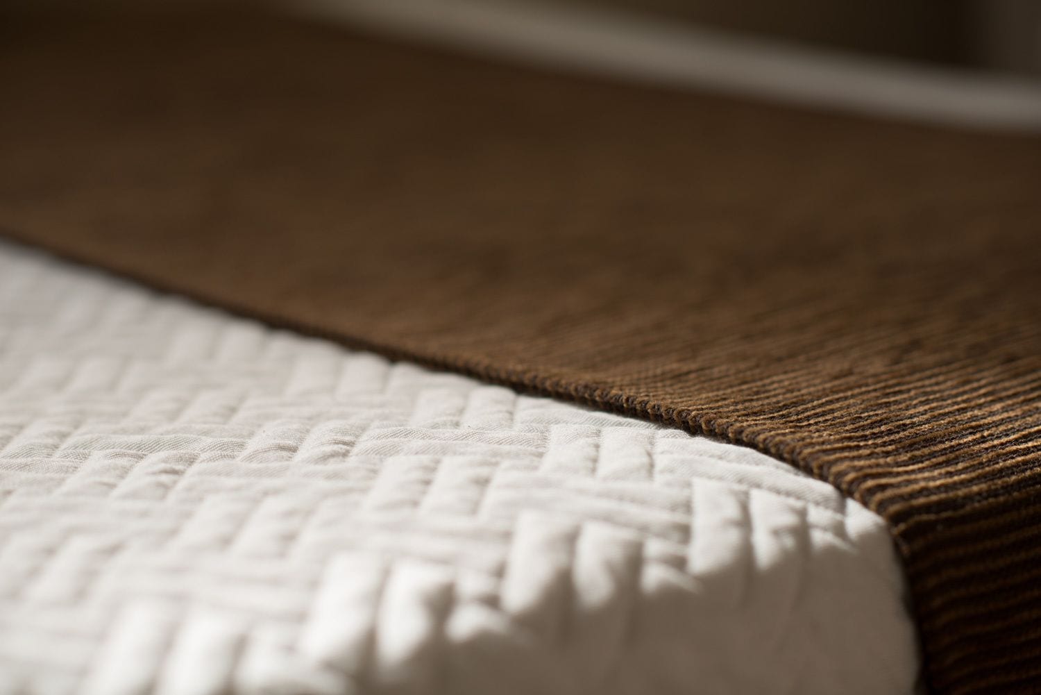 Primer plano de una cama con un colchón blanco texturizado y un cabecero marrón.