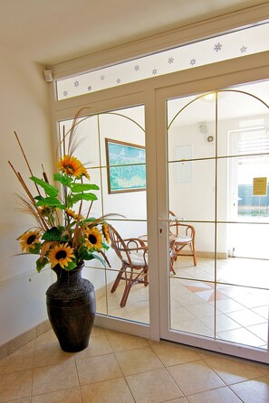 A room with a large vase of sunflowers, a wicker chair, and a glass door leading to a balcony. - Penzión Maxim (Liptovsky Mikulas)