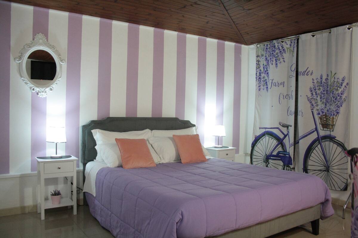 A bedroom with a bed, two bedside tables, a mirror, and a bicycle in the background.