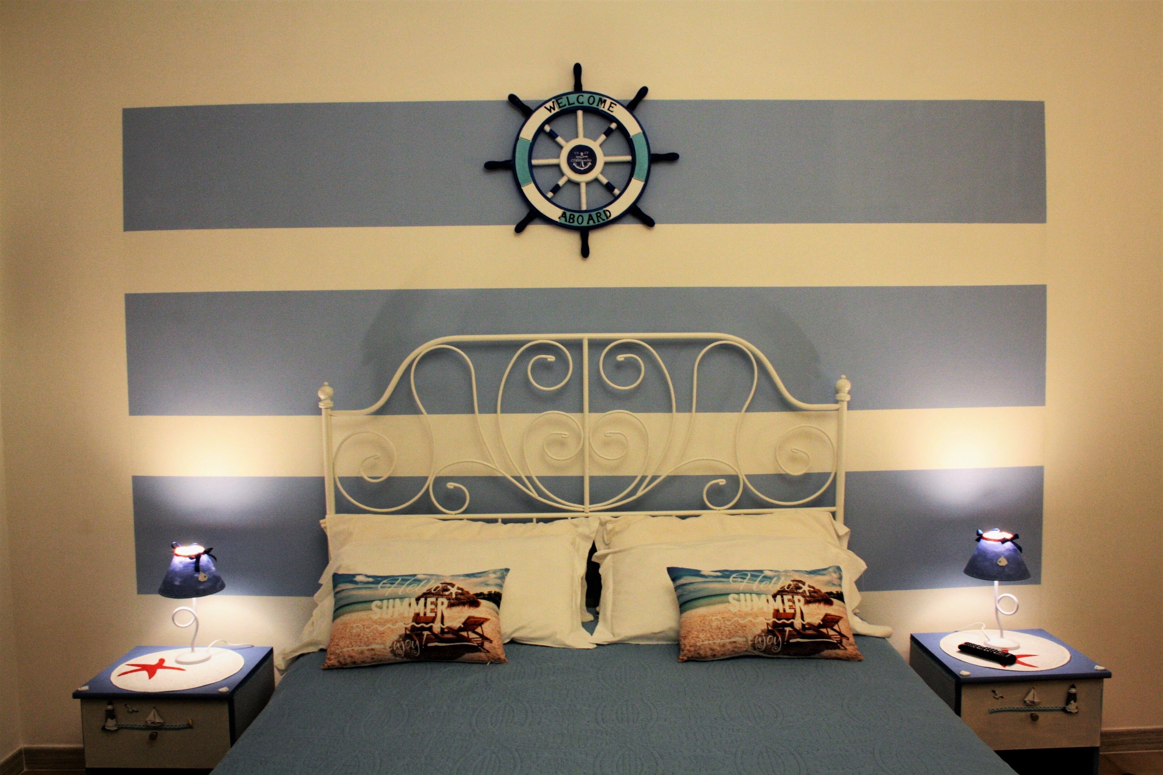 A bed with a striped headboard, two bedside lamps, and a ship's wheel decoration above it.