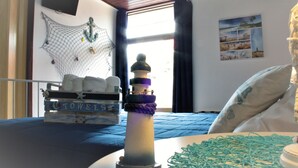 Una habitación con una cama, una lámpara, un televisor instalado en la pared, una ventana con cortinas y una pared decorada con un cuadro.