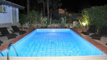 Piscina rectangular con borde de azulejos, rodeada de sillas de descanso y plantas en macetas.