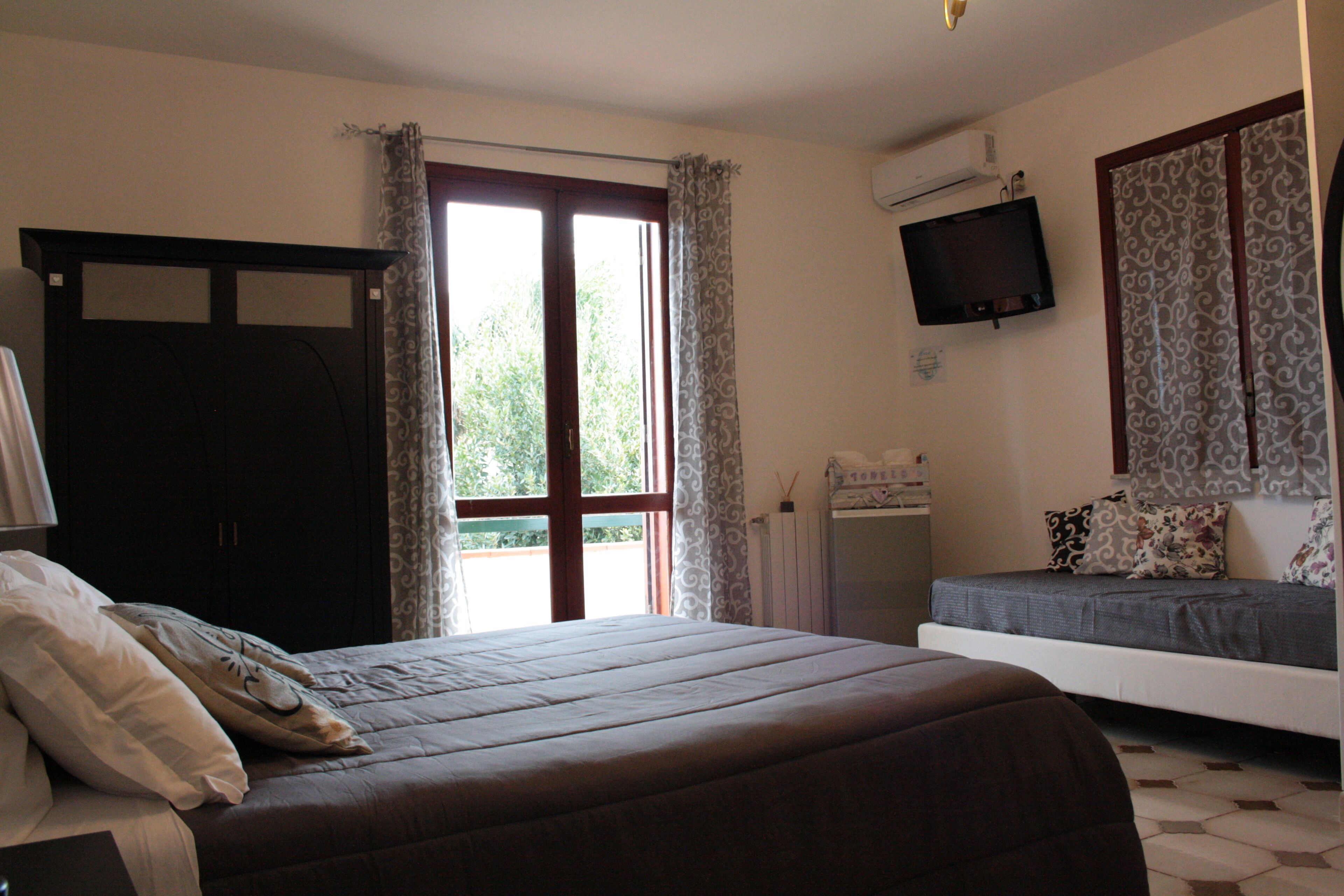 A bedroom with a bed, a sofa, a TV, and a window with curtains.