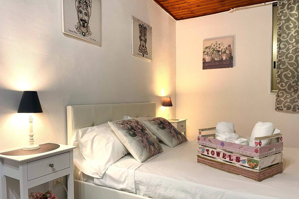 A neatly arranged bedroom with a bed, bedside tables, a lamp, and a box of towels.