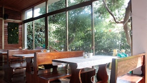 Un restaurante con bancos y mesas de madera, ventanas amplias y vistas a árboles.