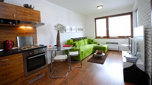 A compact kitchen with modern appliances, a dining area with a green sofa, and a large window providing natural light.