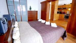 A bedroom with a large bed, a desk with a computer, and a sliding door leading to a kitchen.