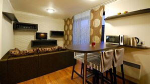 A compact kitchen with a round dining table, two striped chairs, a built-in bench, a TV, a microwave, and a kettle.