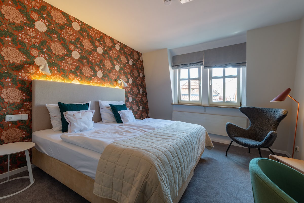 A hotel room with a large bed, a chair, a small table, and a window with a view.