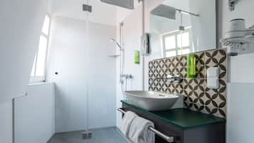 Un baño moderno con cabina de ducha de vidrio, un espejo grande y encimera verde.