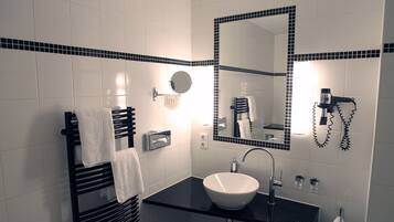 Un baño moderno con lavamanos de superficie negra, un espejo con marco de azulejos negros, un perchero y un secador de pelo en la pared.