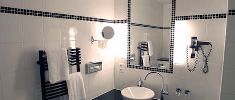 Un baño moderno con lavamanos de superficie negra, un espejo con marco de azulejos negros, un perchero y un secador de pelo en la pared.