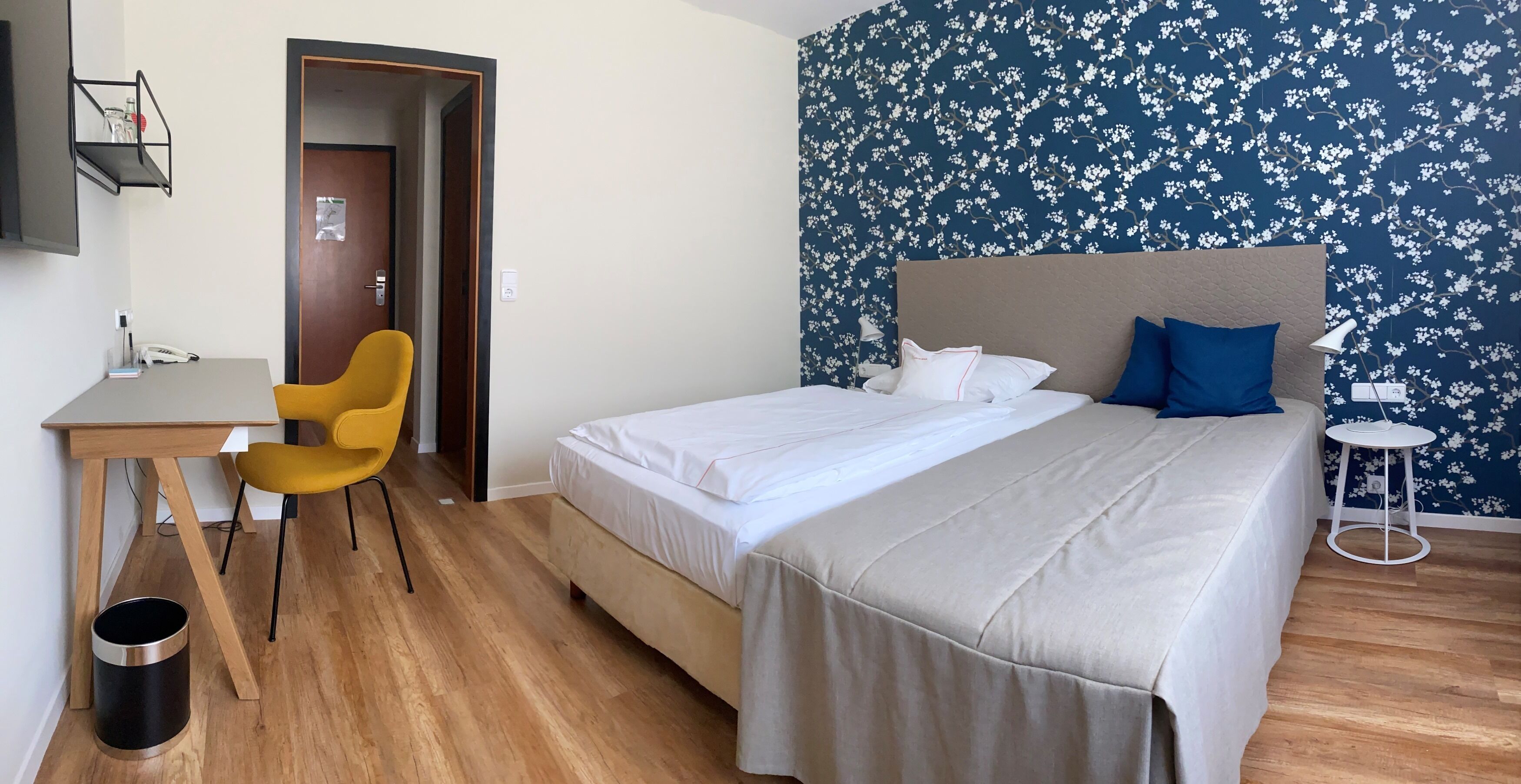 A bedroom with a bed, a desk, a chair, and a small table.