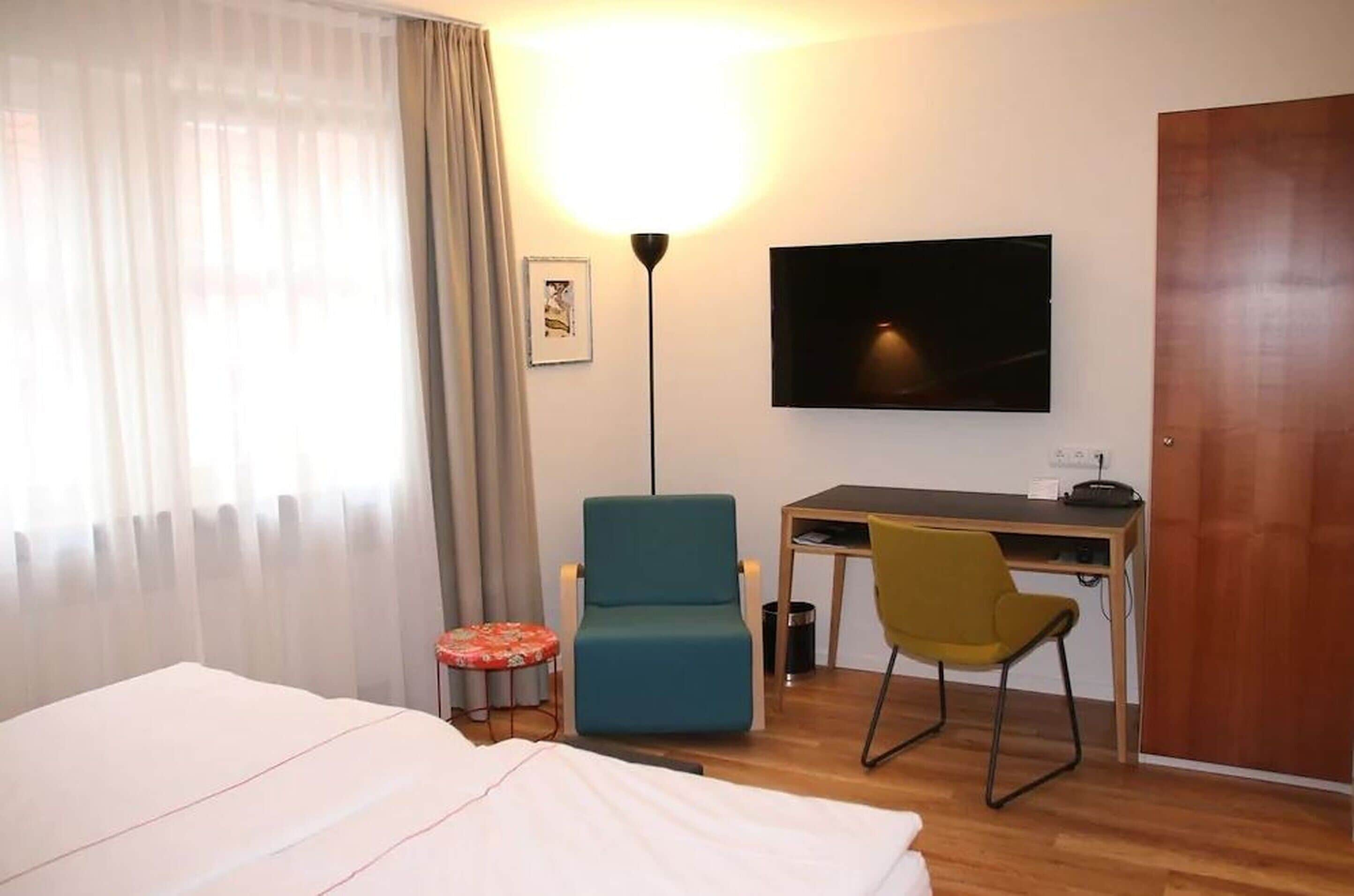 A hotel room with a bed, a desk, a TV, and a chair.