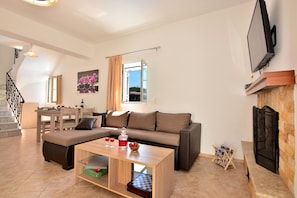 A living room with a sofa, coffee table, and fireplace. There is a television mounted on the wall and a window with curtains.