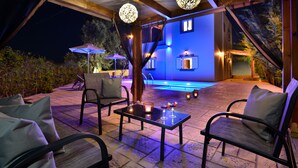 An outdoor patio area with seating, a pool, and ambient lighting. - Elia Villa (Mylopotamos)