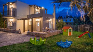 A two-story house with a balcony, a small playhouse, and a slide in the yard. - Elia Villa (Mylopotamos)