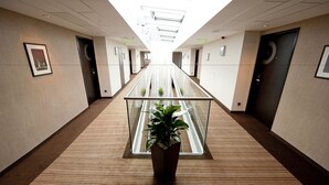 Un pasillo moderno de hotel con barandilla de cristal, una planta en maceta y un techo con tragaluces.