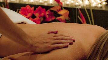 Una sesión de masoterapia en una habitación tenue, con velas y flores.