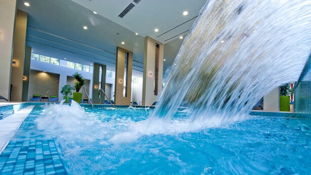 Una piscina interior con una cascada, rodeada de sillones de descanso y plantas en macetas.