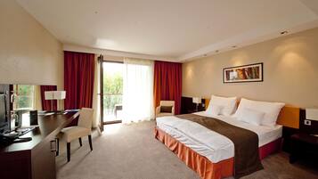 A hotel room with a bed, desk, chair, and a window with curtains.