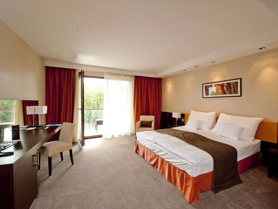 A hotel room with a bed, desk, chair, and a window with curtains.