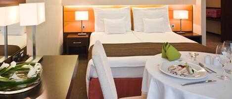 A hotel room with a bed, bedside tables, a dining table with a plate of food, and a vase with flowers.