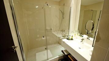 Un baño moderno con ducha de vidrio, un espejo grande y un lavabo blanco con artículos de aseo.