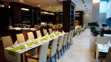 Restaurante com mesas grandes dispostas para refeições, espaço de bar e área de estar com cadeiras e mesas.