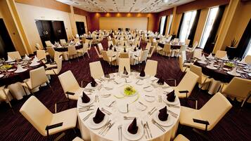 Un amplio salón de banquetes con mesas redondas dispuestas para un evento formal, equipado con sillas, vajilla y un escenario al frente.