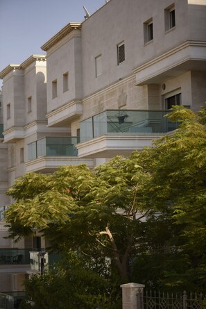 Um edifício de vários andares com varandas, uma árvore em primeiro plano e um céu claro.