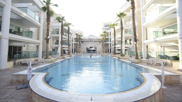 A large indoor swimming pool surrounded by palm trees and modern architecture. - City Resort Palmore (Eilat)