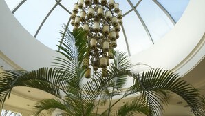 A spacious atrium with a large glass ceiling, palm trees, and a decorative chandelier. - City Resort Palmore (Eilat)