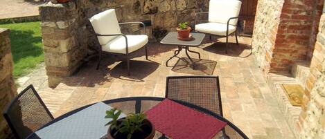 An outdoor patio with stone walls, white chairs, and a table with a red tablecloth.