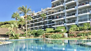 Un hotel de varios pisos con balcones, piscina y jardines tropicales.